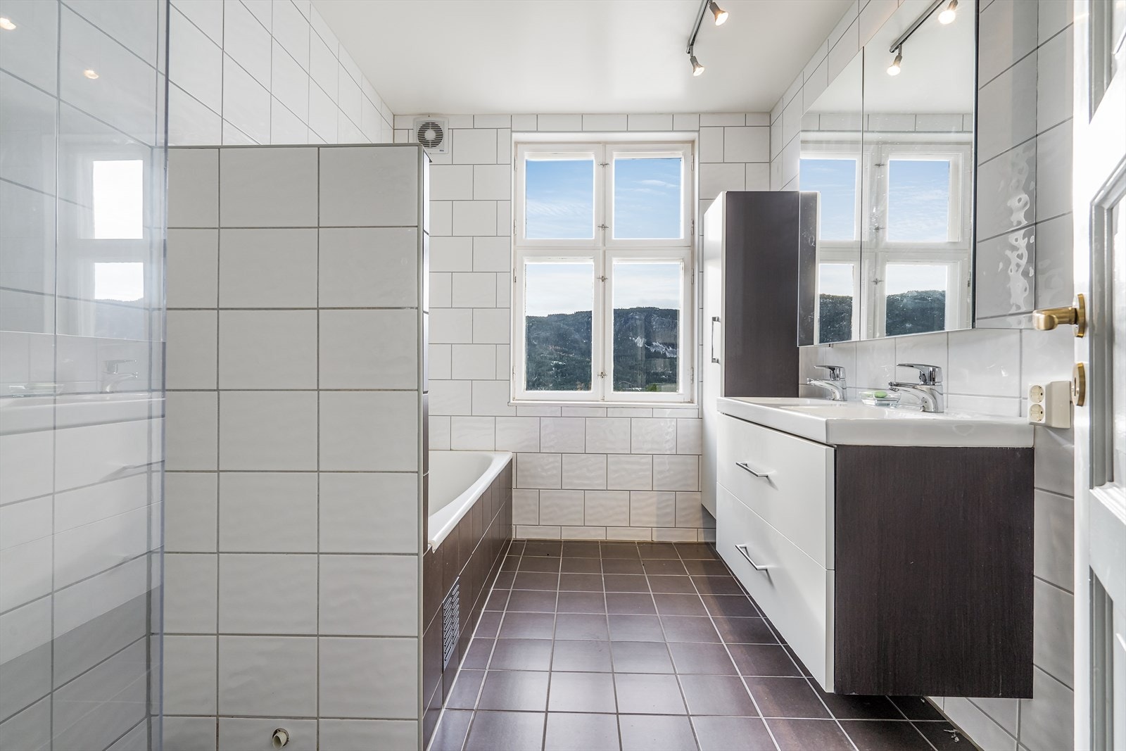 Bad med dusjnisje, badekar, veggmontert vannklosett og servantskap med dobbel porselensservant. Veggmontert speilskap. Galleribilde