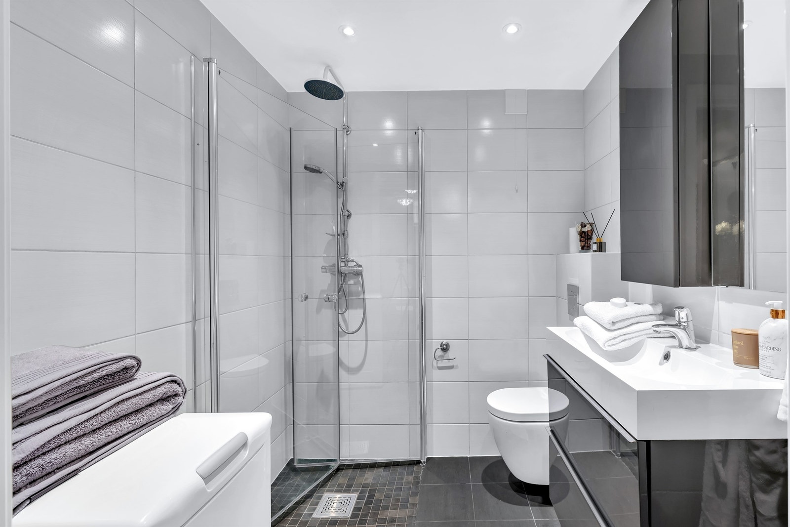 Speil og skap på vegg over servant. Dusjsone med innfellbare dører av glass. Opplegg for vaskemaskin. Galleribilde