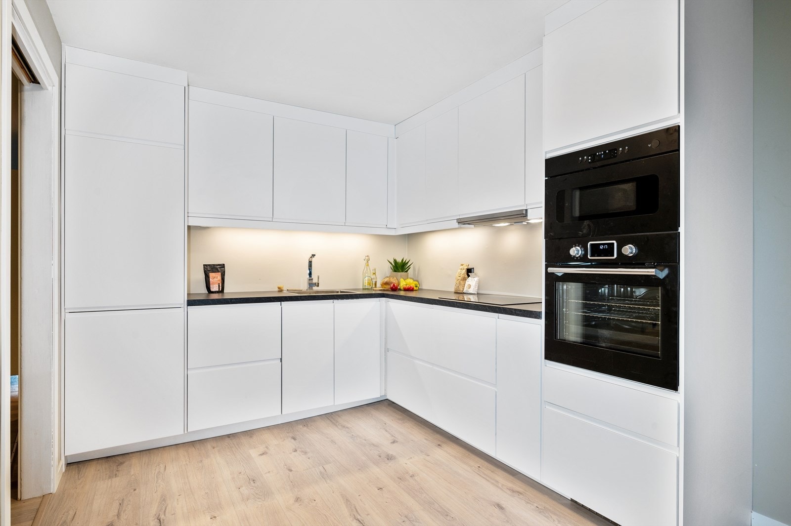 Det separate kjøkkenet er ved totalrehabiliteringen holdt lyst, lekkert og luftig. Innredningen består av hvit plan kjøkkeninnredning med mørk laminert benkeplate og nedfelt oppvaskkum. Galleribilde