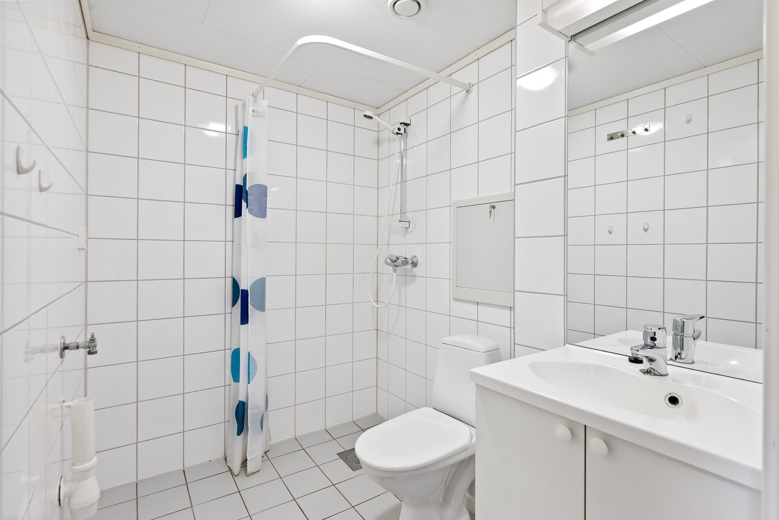 Praktisk bad med innredning med servant, wc og dusj på vegg med forheng. Her er det også opplegg for vaskemaskin. Galleribilde