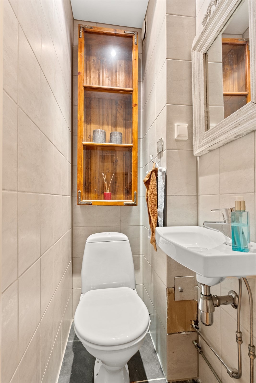 Separat WC med flis på gulv og vegg. Innredet med hyller på vegg, servant, speil over servant og gulvmontert toalett. Downlights i himling. Galleribilde