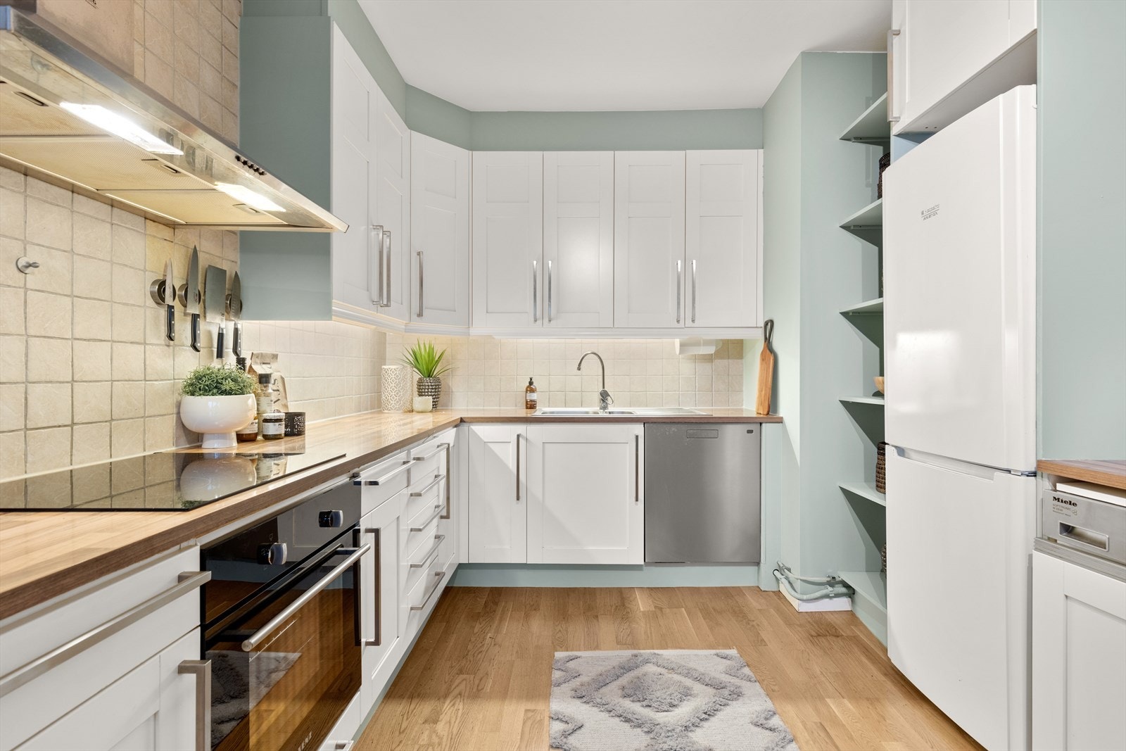 Kjøkkeninnredningen har hvite profilerte fronter, fliser over laminert benkeplate med nedfelt 1-1/2 oppvaskkum og 1 greps blandebatteri. Avtrekksvifte med kullfilter. Lys under overskapene. Opplegg for oppvaskmaskin. Galleribilde