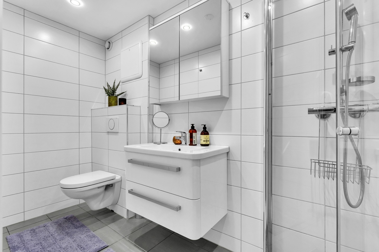 Det andre badet ligger i behagelig løsning med ett soverom. Det er holdt i et tidløst design med hvite veggfliser og grå gulvfliser Galleribilde