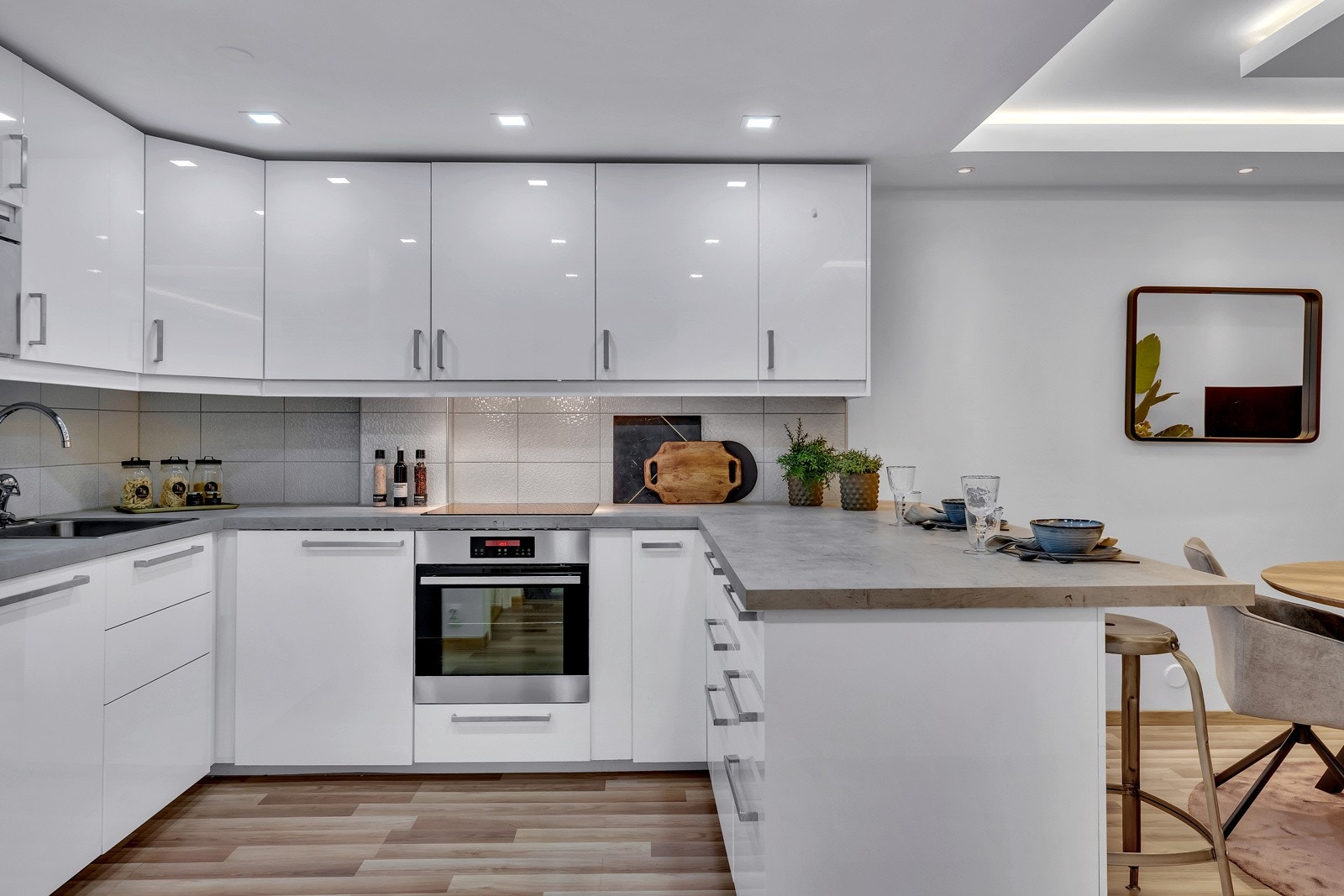 Innredningen har takhøye skap, hvite høyglansfronter og grå laminatbenkeplate med nedfelt oppvaskkum Galleribilde