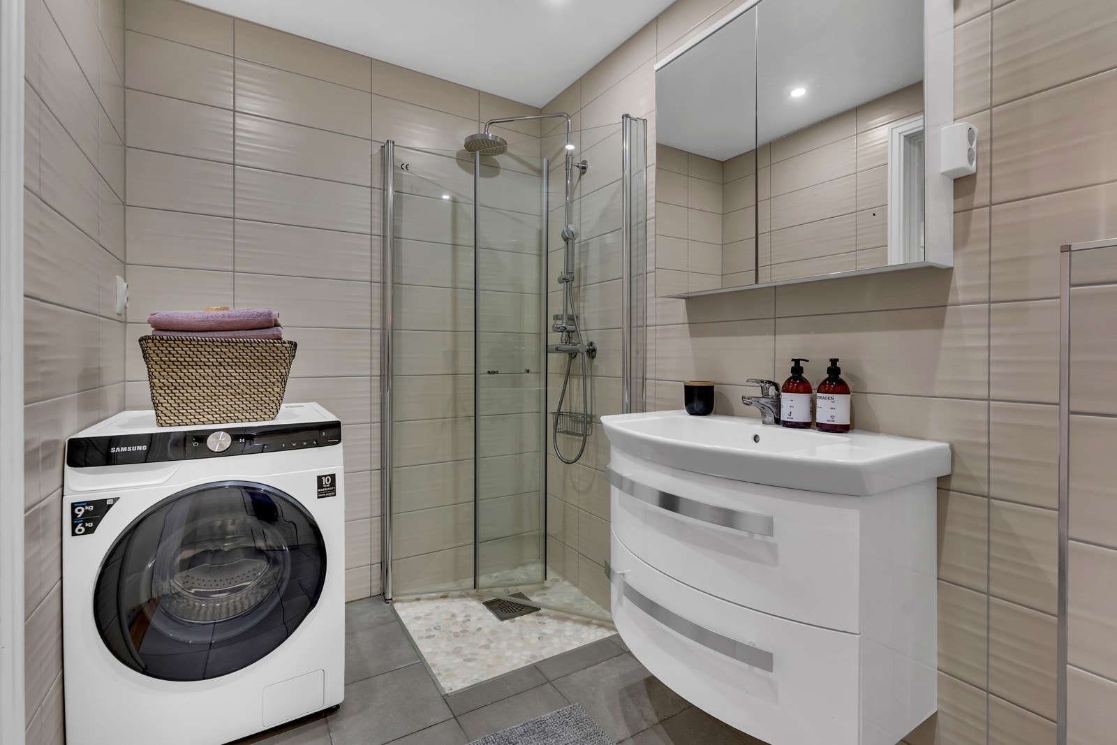 Himling er pent lyssatt med downlights og det er veggmontert toalett. I hjørnet ved siden av dusjen er det opplegg for vaskemaskin Galleribilde