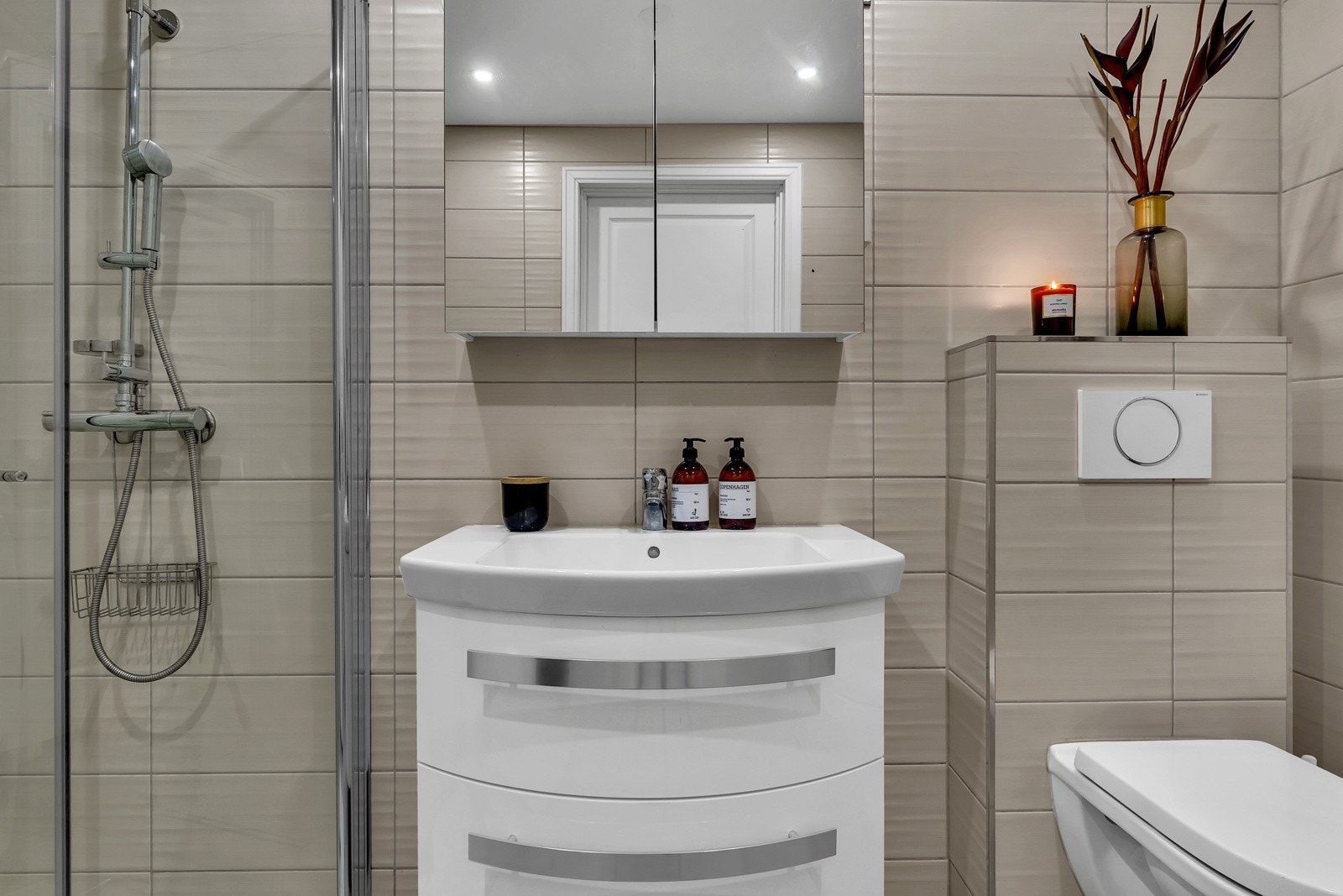 Hovedbadet ligger i tilknytning til entreen og er stilfullt innredet med beige veggfliser, og grå gulvfliser som erstattes med hvit rullestein i dusjhjørnet Galleribilde