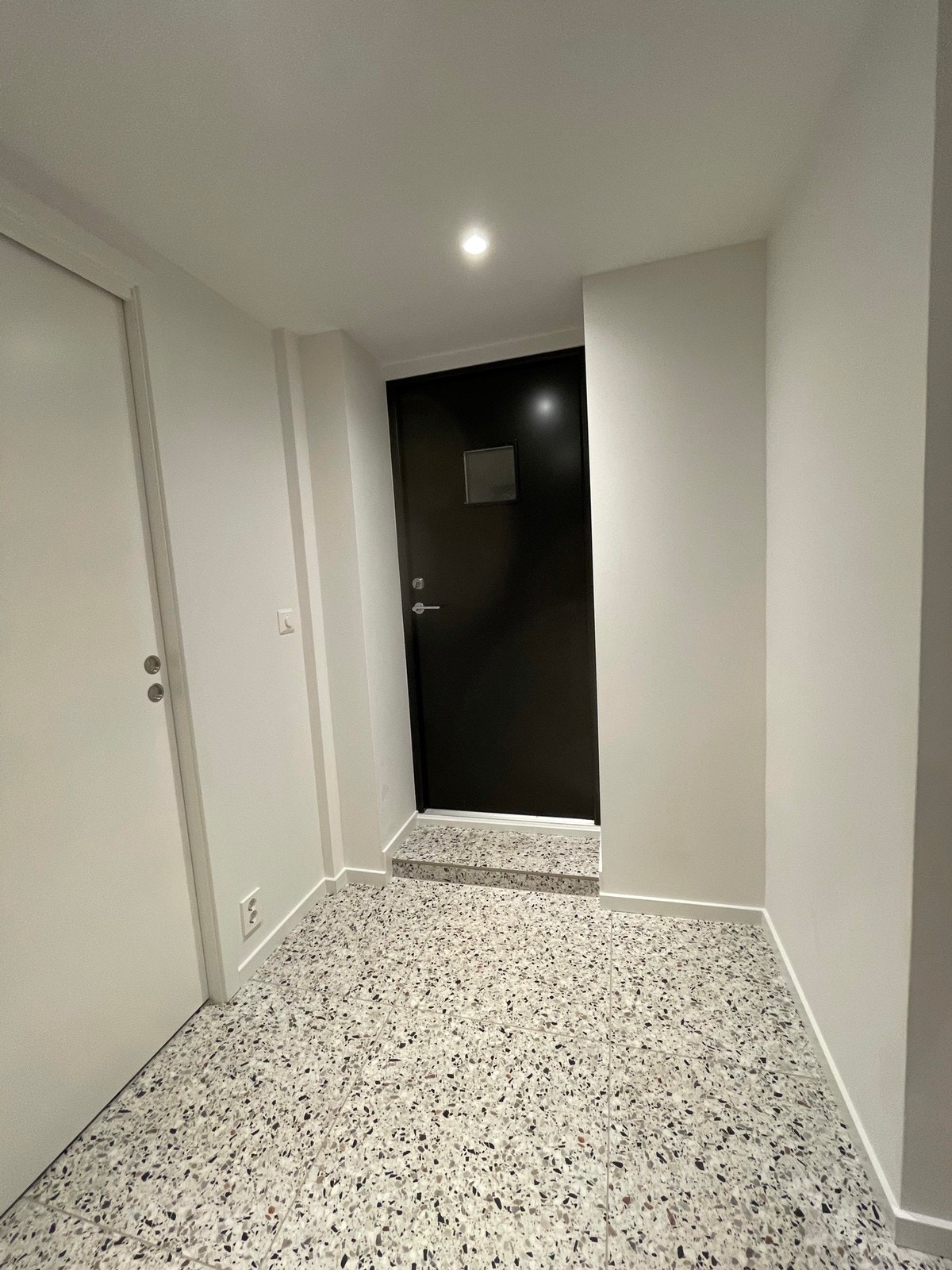 Gang med moderne terrazzo-fliser og egen inngangsdør. Skyvedør til soverom på venstre side. Stue/kjøkkenløsning inn til høyre Galleribilde