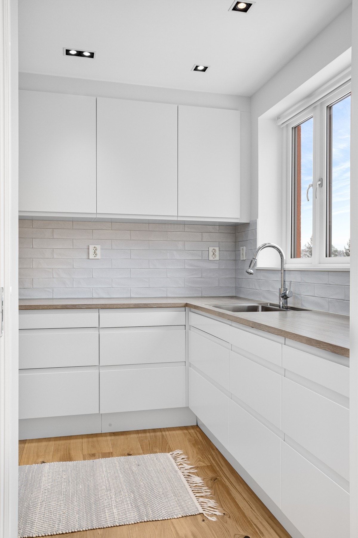 Det er god arbeidsplass langs laminerte benkeplater med underlimt oppvaskkum. Mellom benk og skap er det hvite fliser. Galleribilde