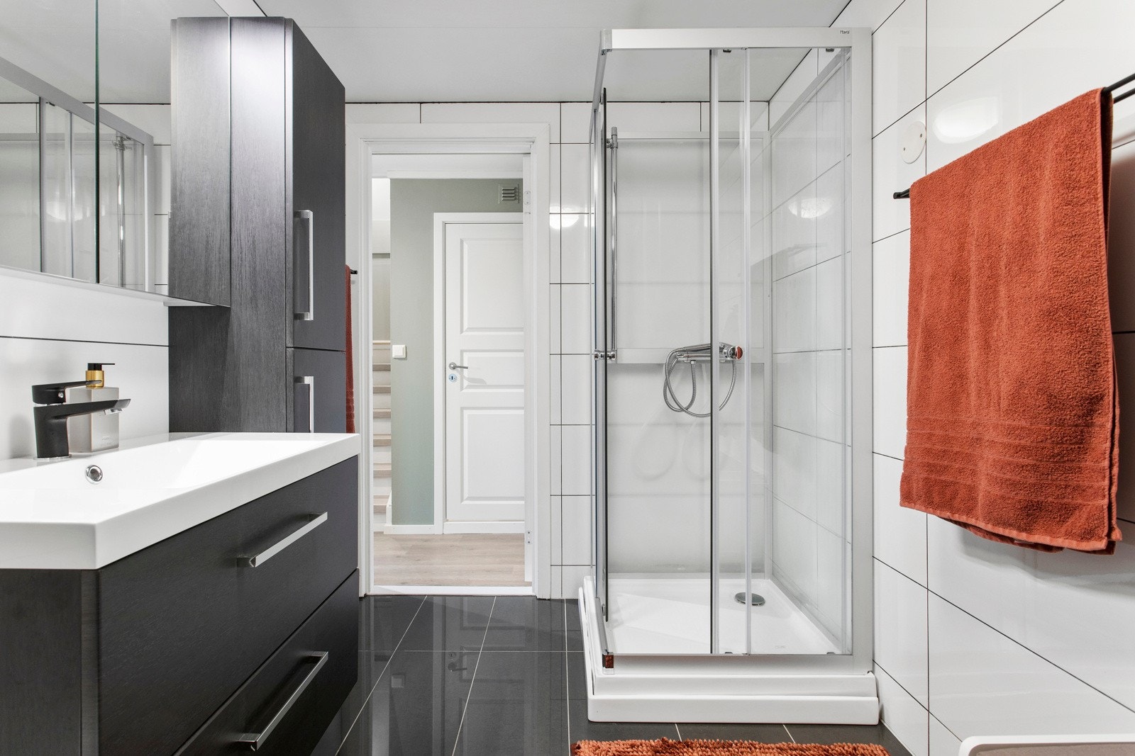 Pent baderom med delikate, mørke gulvfliser med varme, hvite veggfliser og en kontrastvegg med mosaikkfliser. Galleribilde