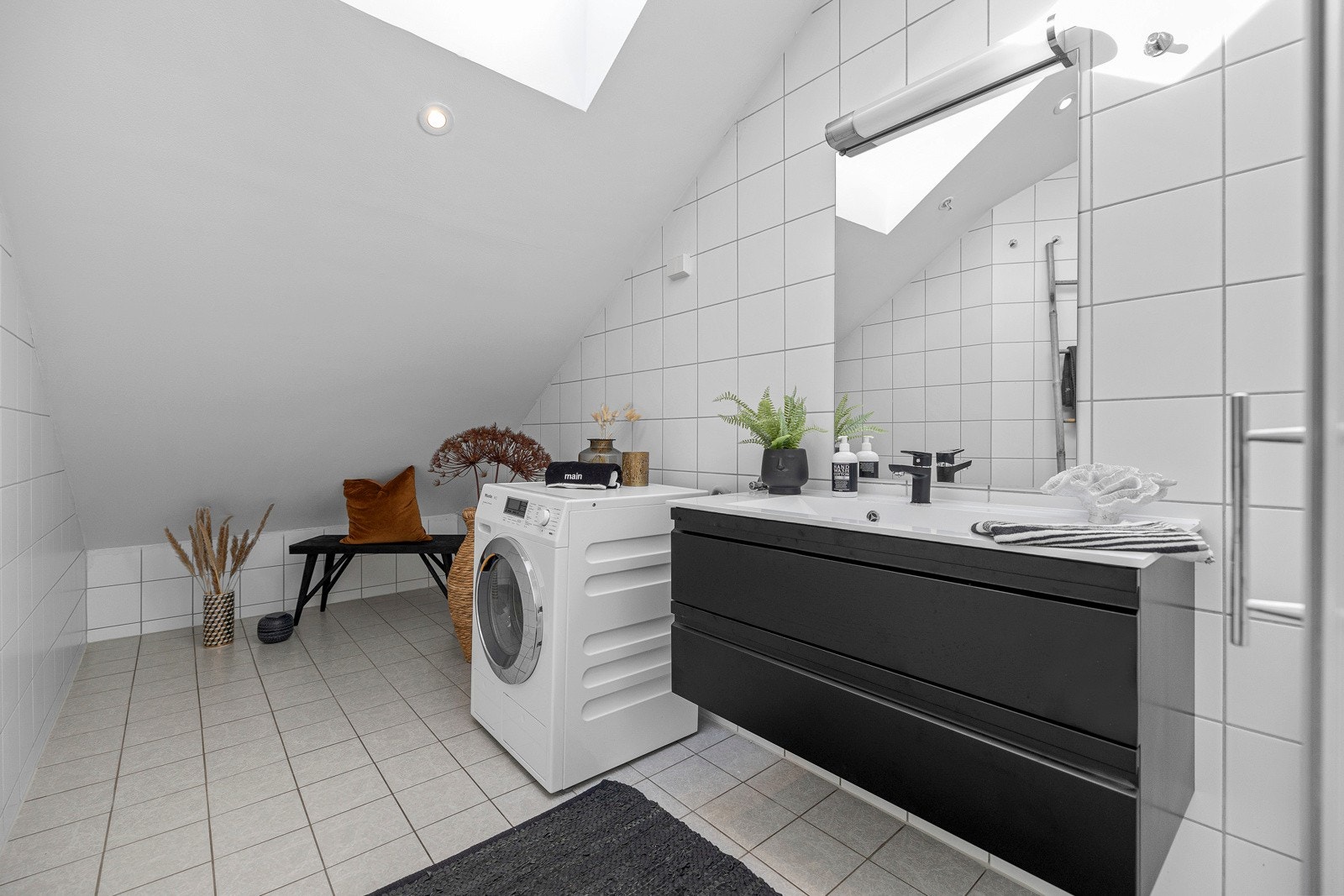 Den mørke baderomsinnredningen har glatte skuffefronter, heldekkende servant og speil med lys i overkant. Galleribilde