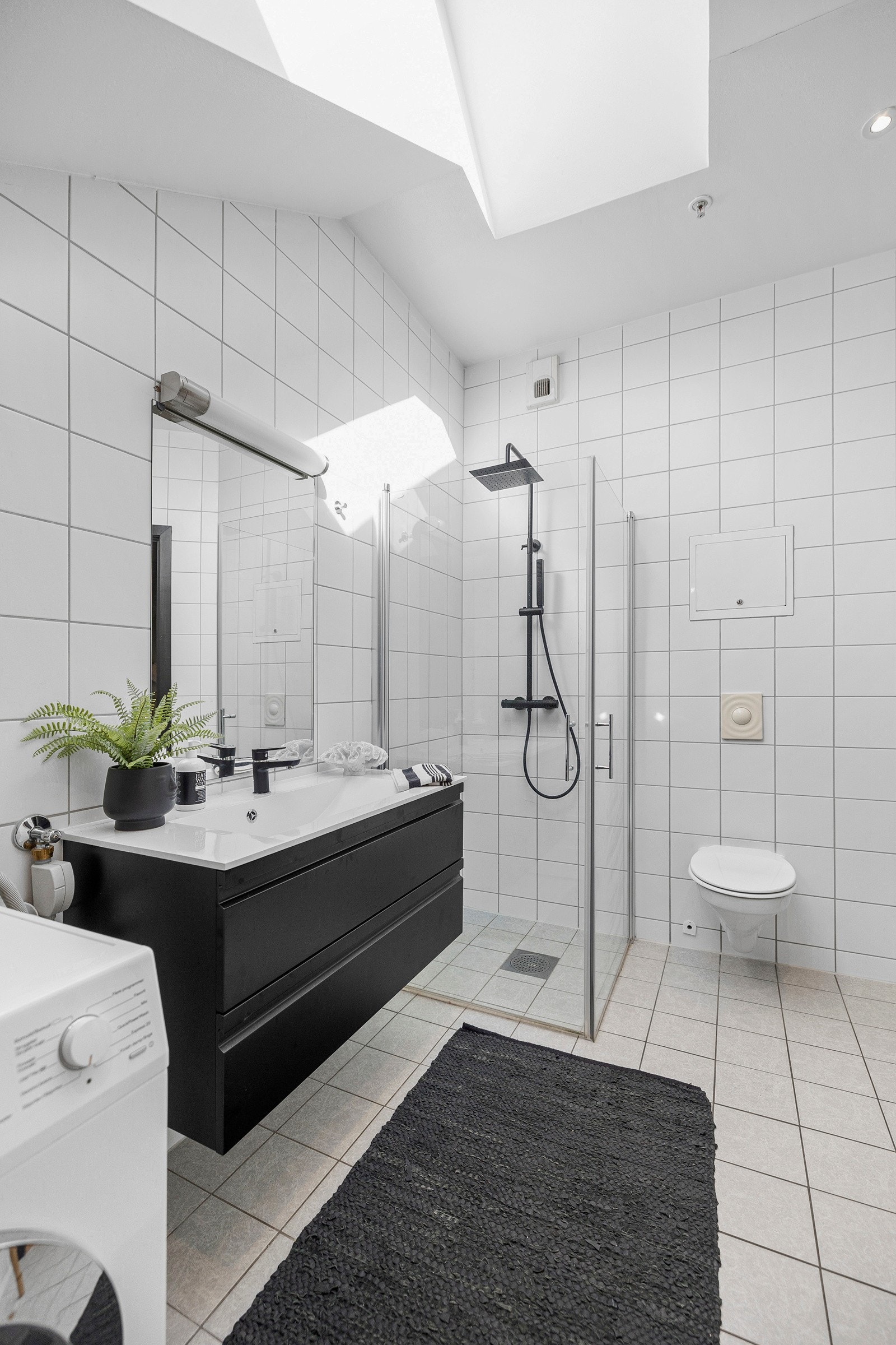 Badet er utstyrt med veggmontert toalett, dusjhjørne med regnfallsdusj, og opplegg for vaskemaskin. Galleribilde