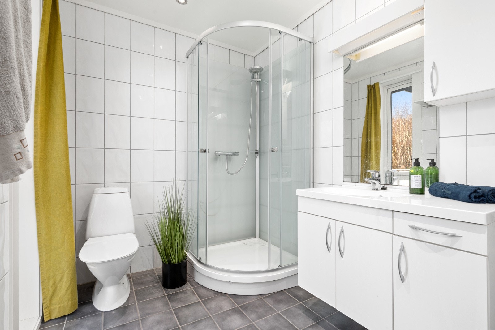 Badet har flis på gulv og vegger og er utstyrt med dusjkabinett, WC og baderomsinnredning med overskap og speil. Galleribilde