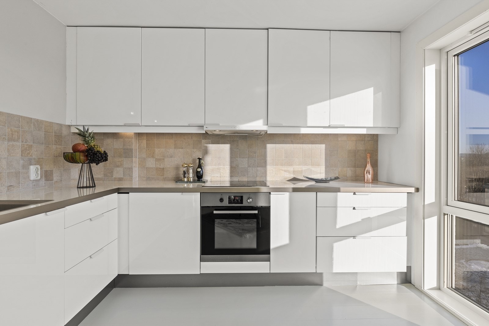 IKEA kjøkkeninnredning fra 2010 med laminerte slette fronter i hvit høyglans, fliser over laminert benkeplate med enkel oppvaskkum og 1-greps blandebatteri. Galleribilde