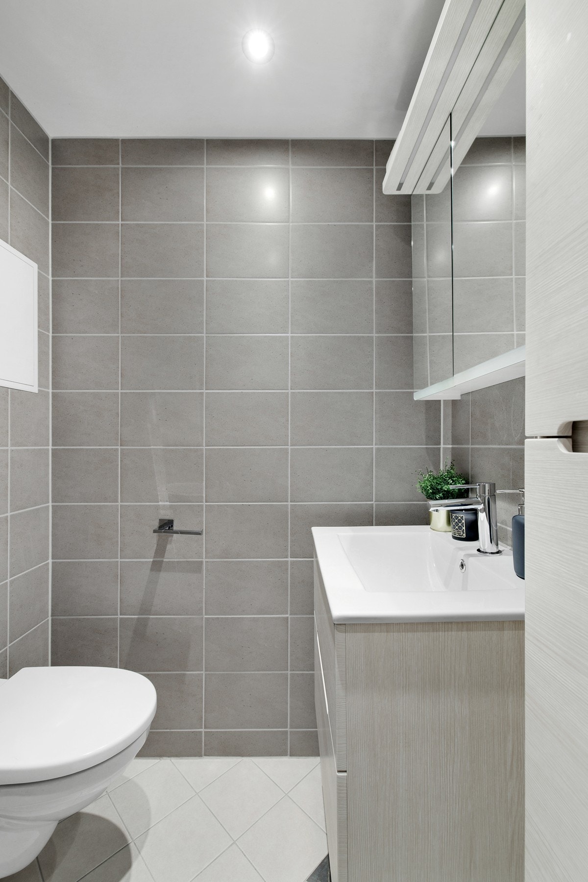 Badet har dusjhjørne med glassdør, servantskap, speilskap og vegghengt toalett Galleribilde