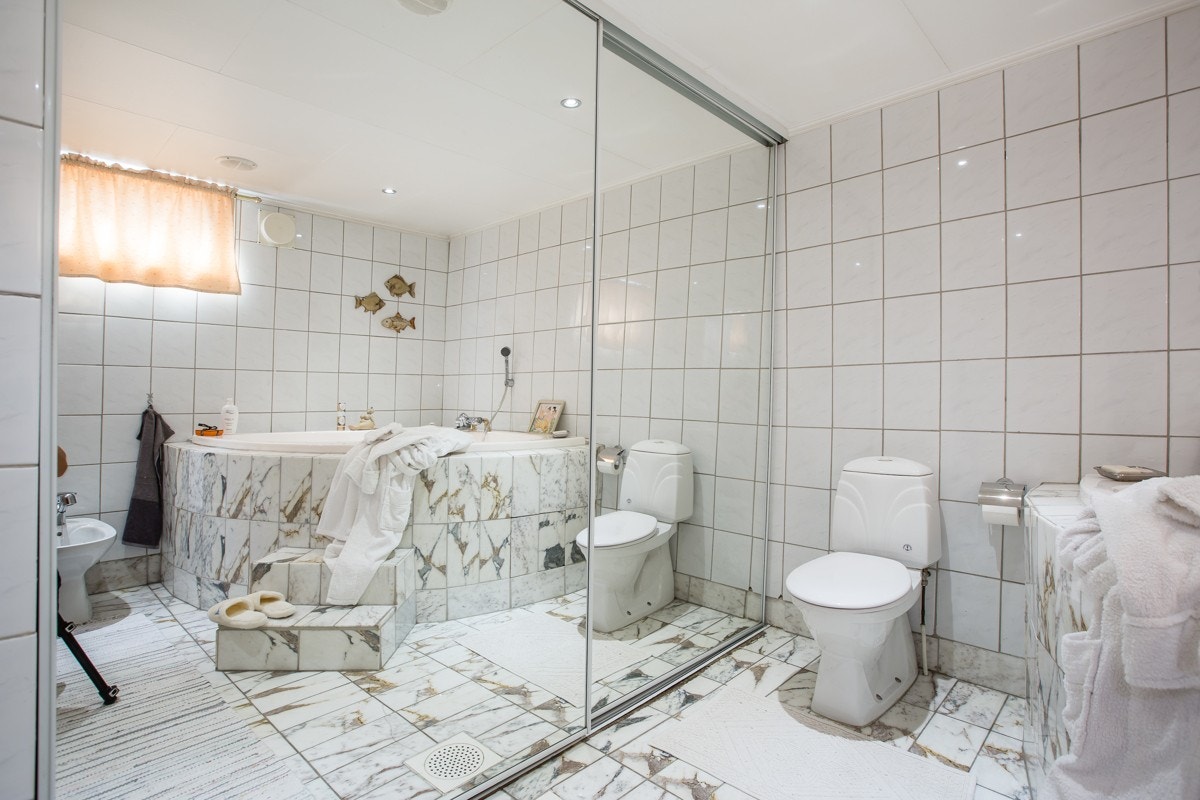 Badet er flislagt med termostatstyrte varmekabler i gulv. Det er opplegg for vaskemaskin og tørketrommel bak den store skyvedøren. Galleribilde