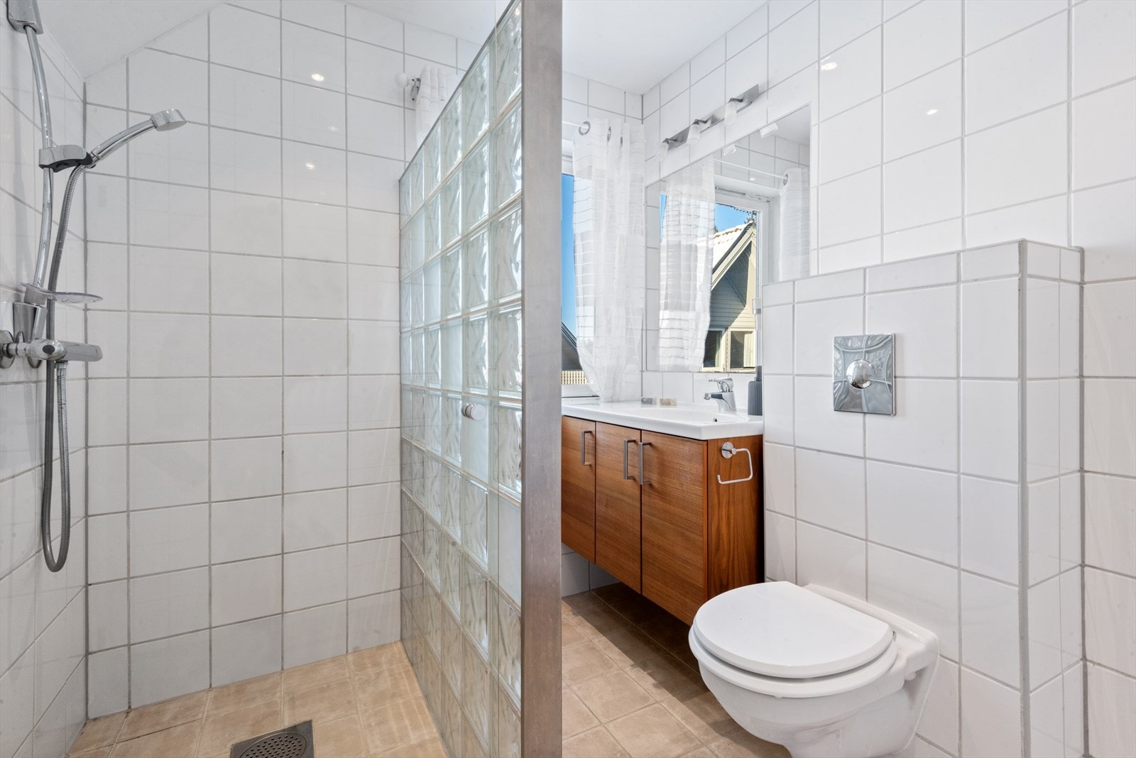 Videre er badet utstyrt med vegghengt toalett og dusjhjørne med dusjvegg i glassblokker. Galleribilde