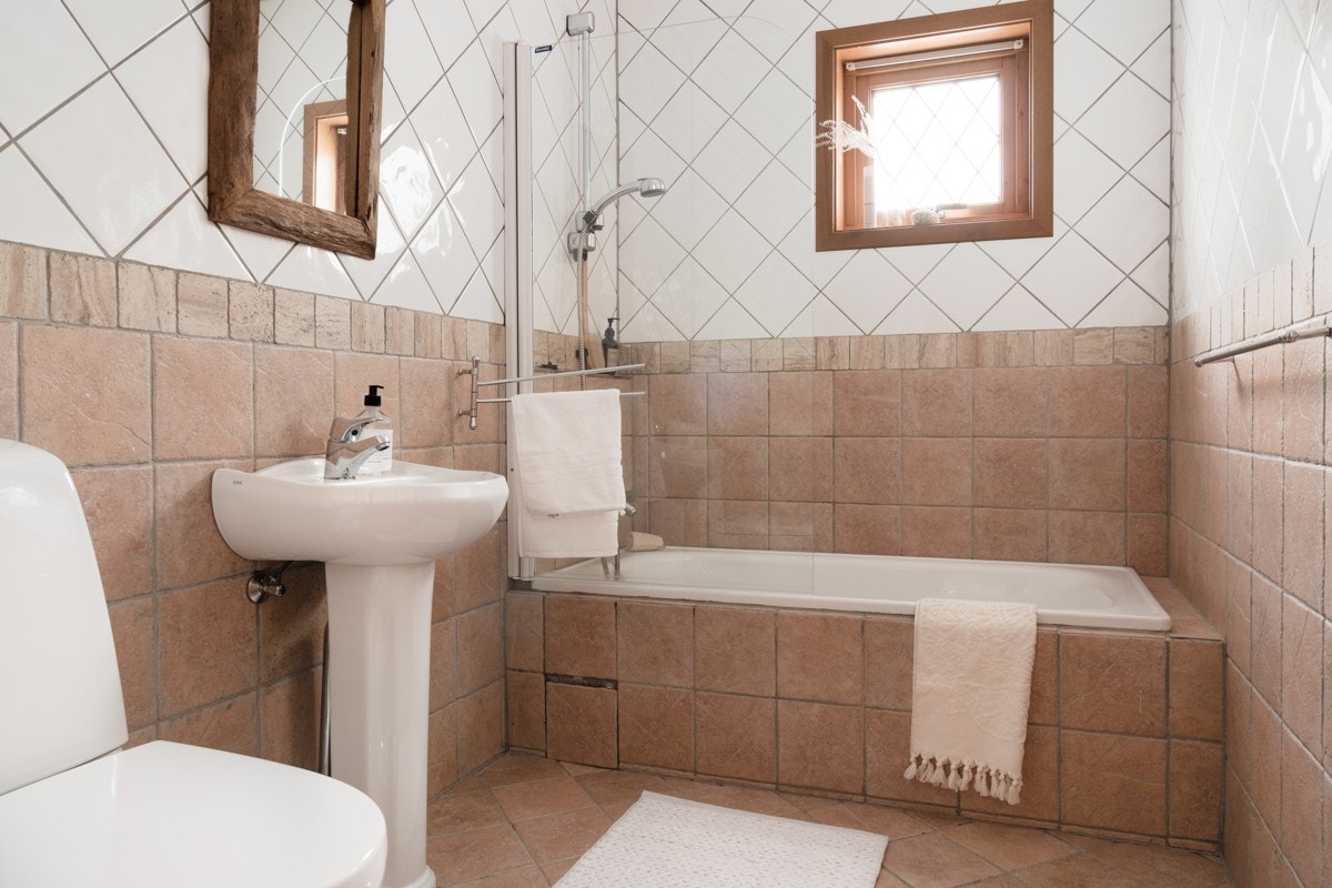 Det er tilkomst til sluk via åpen flis på badekaret. Ellers inneholder badet inneholder toalett, servant og innfliset badekar med dusj. Galleribilde