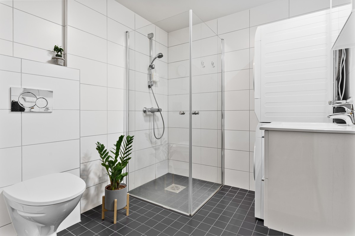 Badet er av fin størrelse og har vegghengt toalett, dusj med glassdører og servant med tilhørende skuffer og speilskap