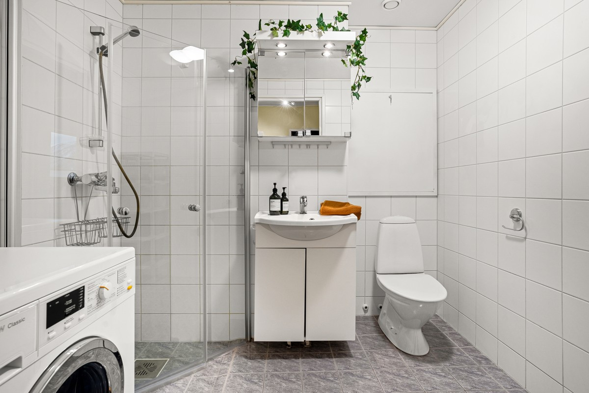 Badet er flislagt og utstyrt med dusjhjørne med innfellbare glassdører, gulvmontert wc, opplegg for vaskemaskin, samt baderomsinnredning med servant og skap.
