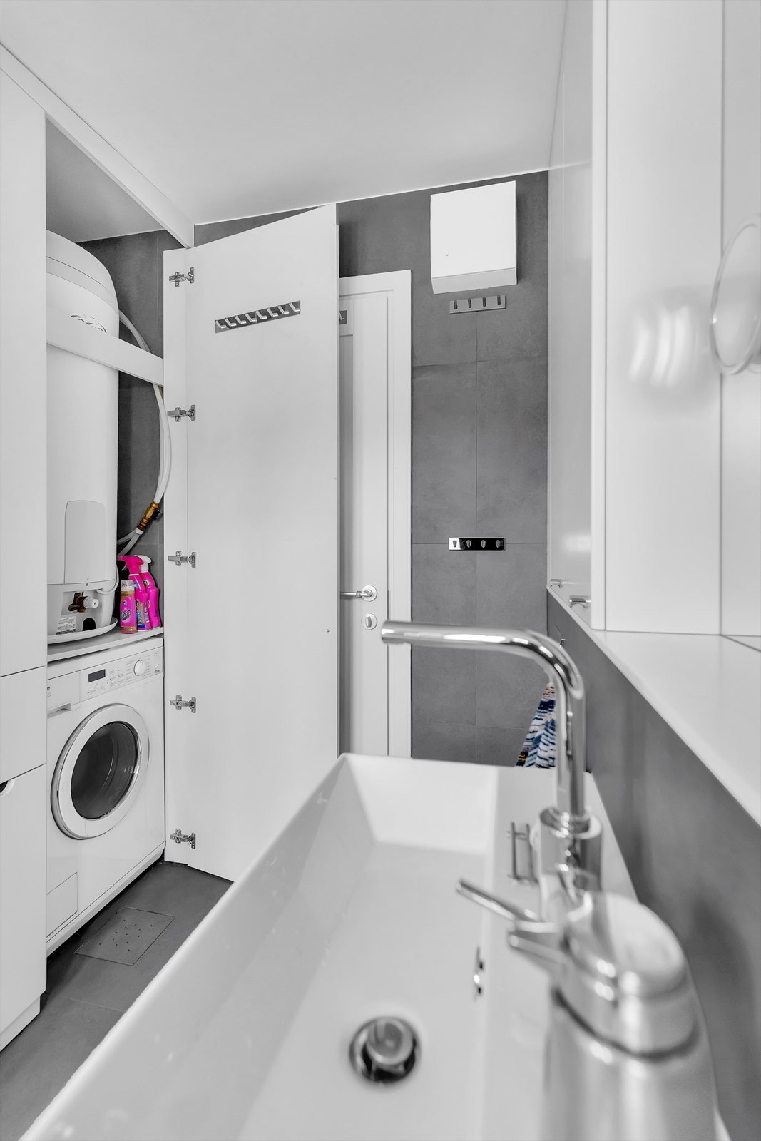 Plassbyggede skap med varmtvannsbereder, og Miele kombinert vask/tørkemaskin. Skapet ved siden av har innebygget skittentøyskurv. Galleribilde