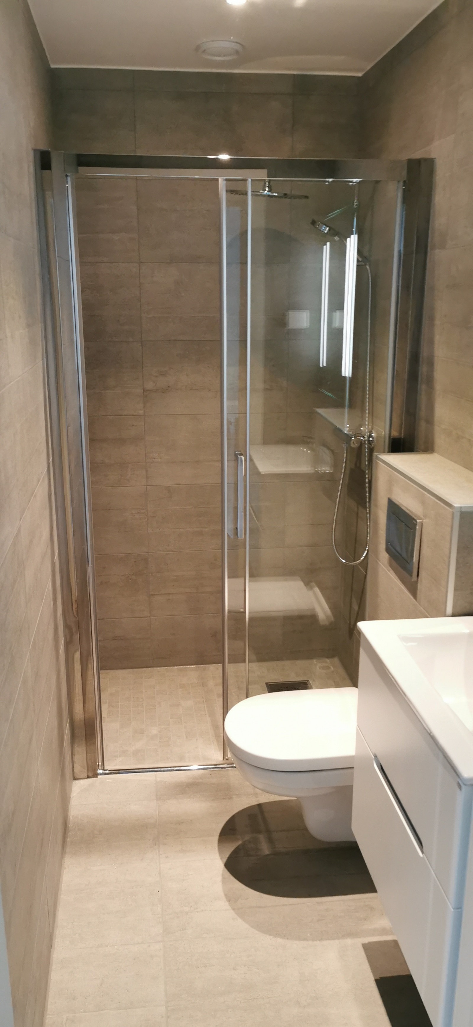 Oppdatert bilde av bad. Grå fliser på vegg og gulv. Galleribilde