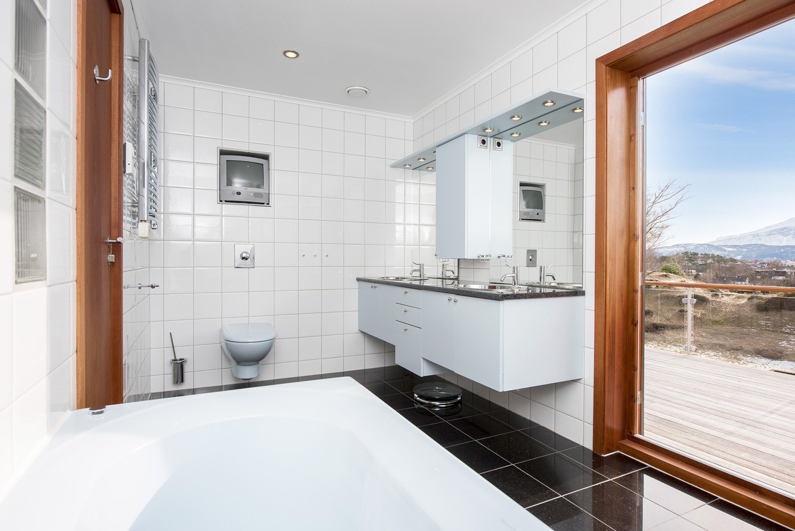 Flislagt bad med dør til teak terrasse. Spesialtilpasset baderomsinnredning fra HTH med sanitærutstyr fra Villeroy & Boch og Vola Galleribilde