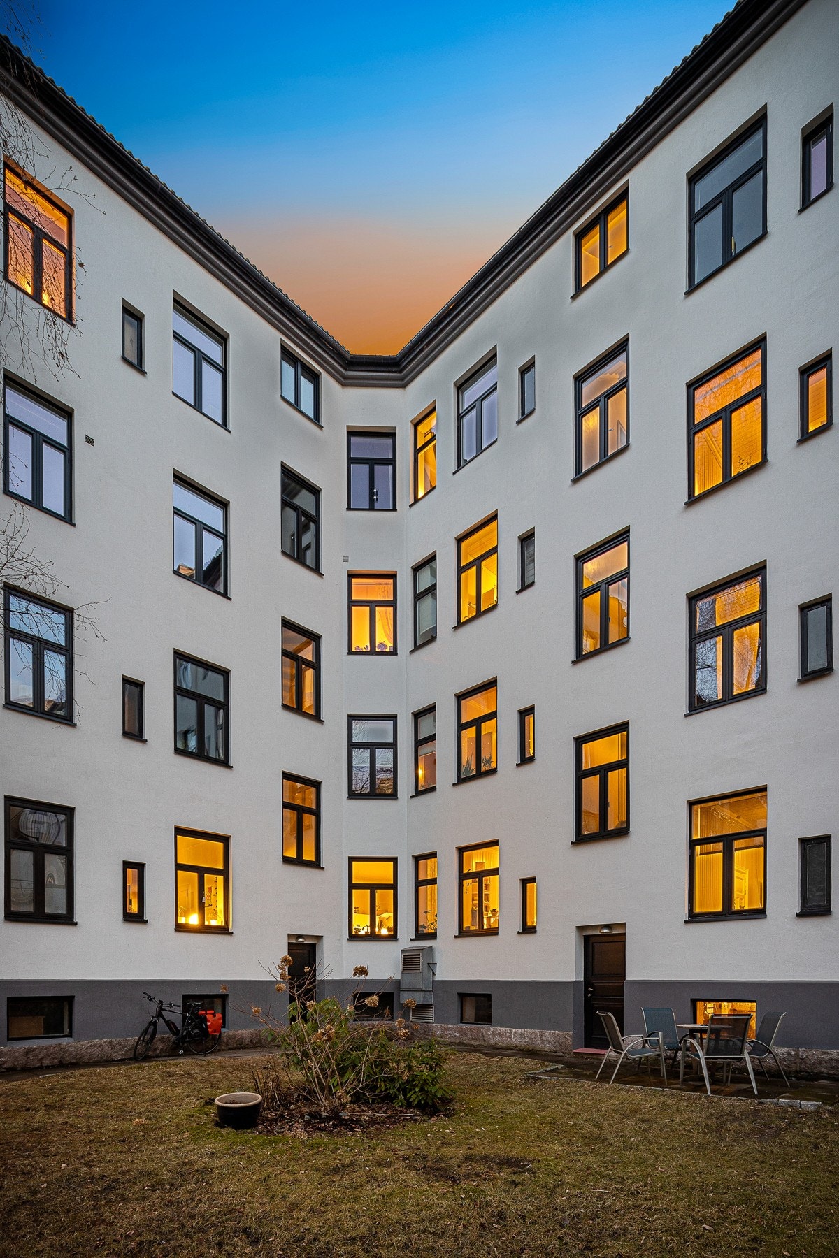 Skjermet og koselig bakgård med hellebelagt uteplass og beplantet med plen og diverse beplantning Galleribilde