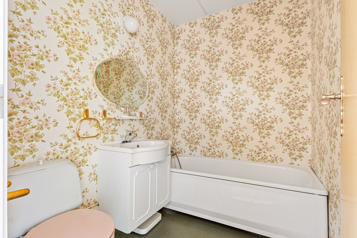 Badet har gulvbelegg, tapet, toalett og badekar med dusjgarnityr. Galleribilde