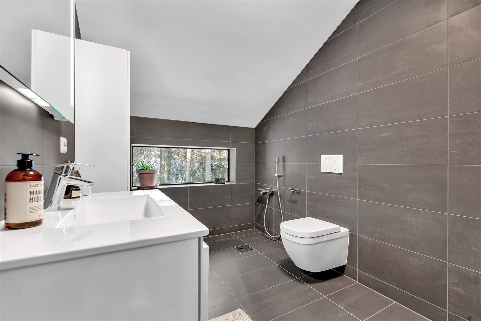 Badet tilknyttet hovedsoverommet er pent flislagt med mørke avlange fliser. Det er ferdigmontert armatur for badekar og klargjort sluk for dette. Galleribilde