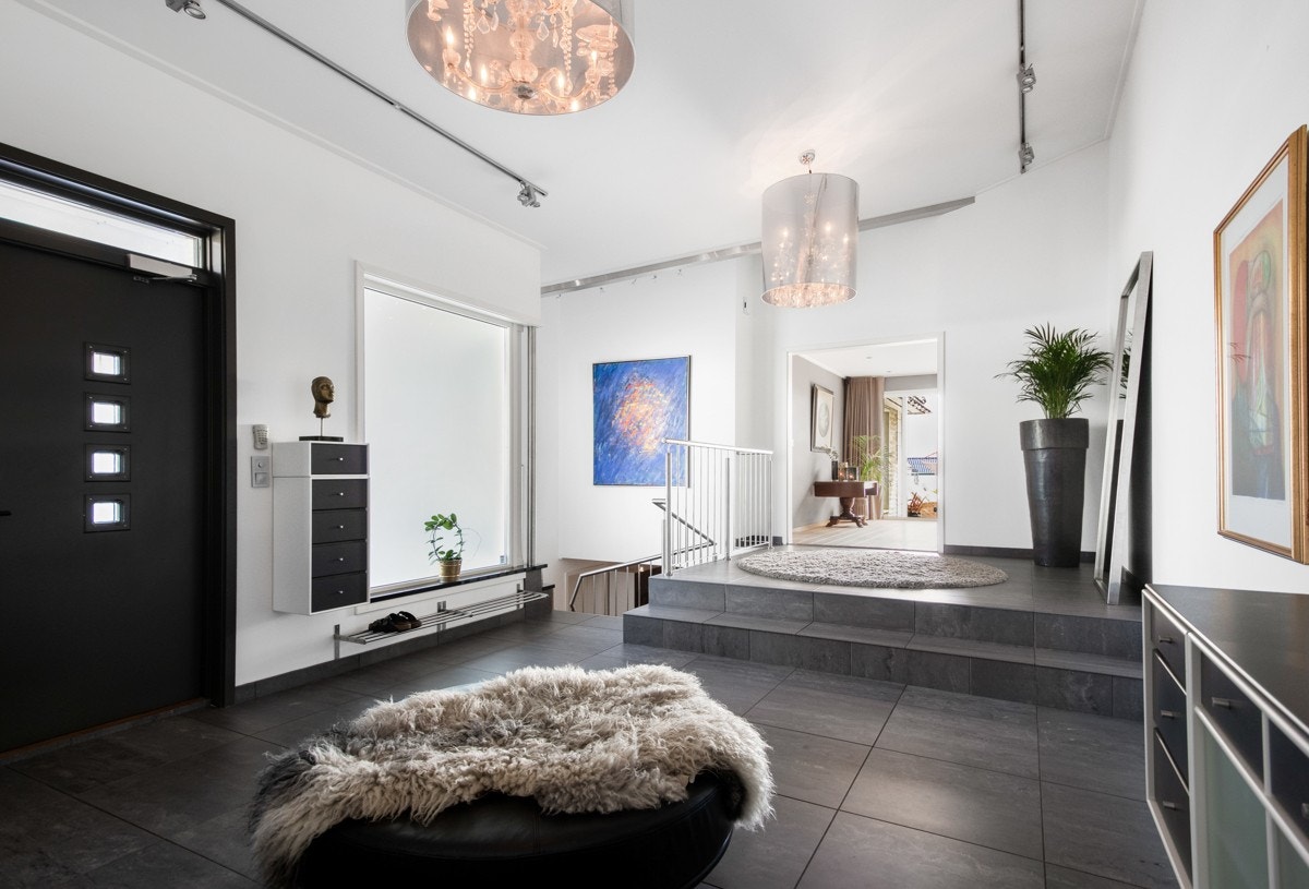 En tofløyet ytterdør fører inn i hallen med fliser, lysmalte vegger og vannbåren gulvvarme. Galleribilde