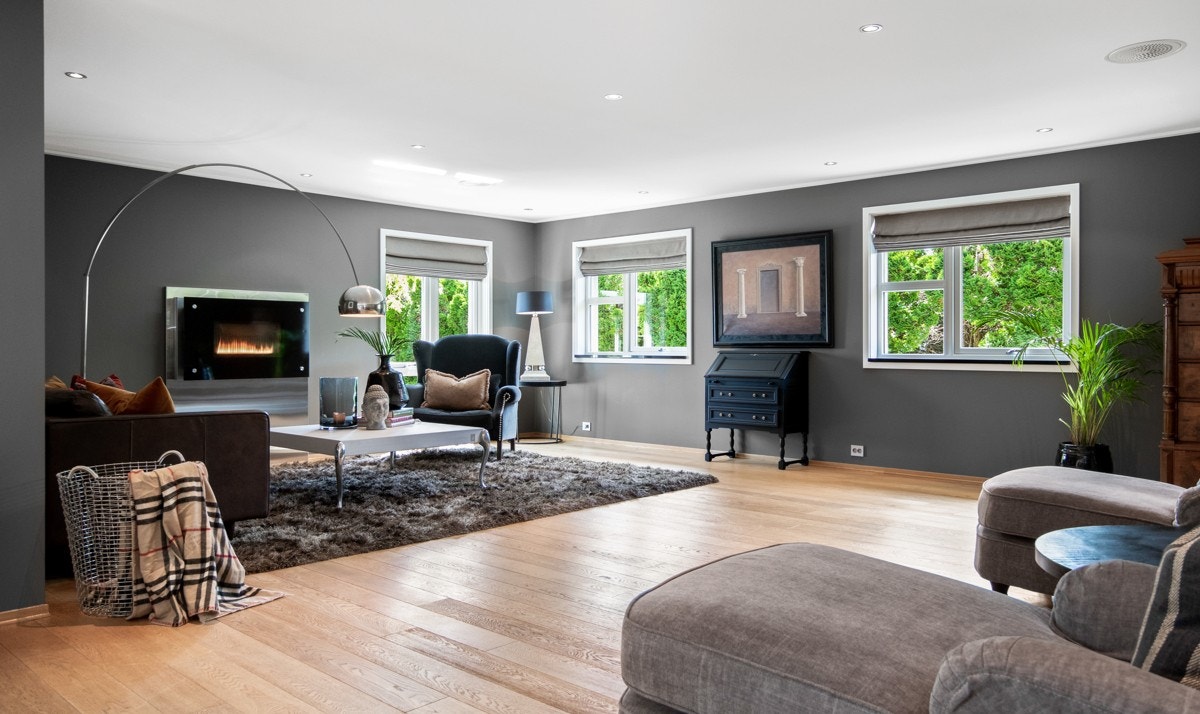 Vindusflatene fyller rommet med dagslys fra flere retninger, og selve blikkfanget er en elegant gasspeis med bred omramming. Galleribilde