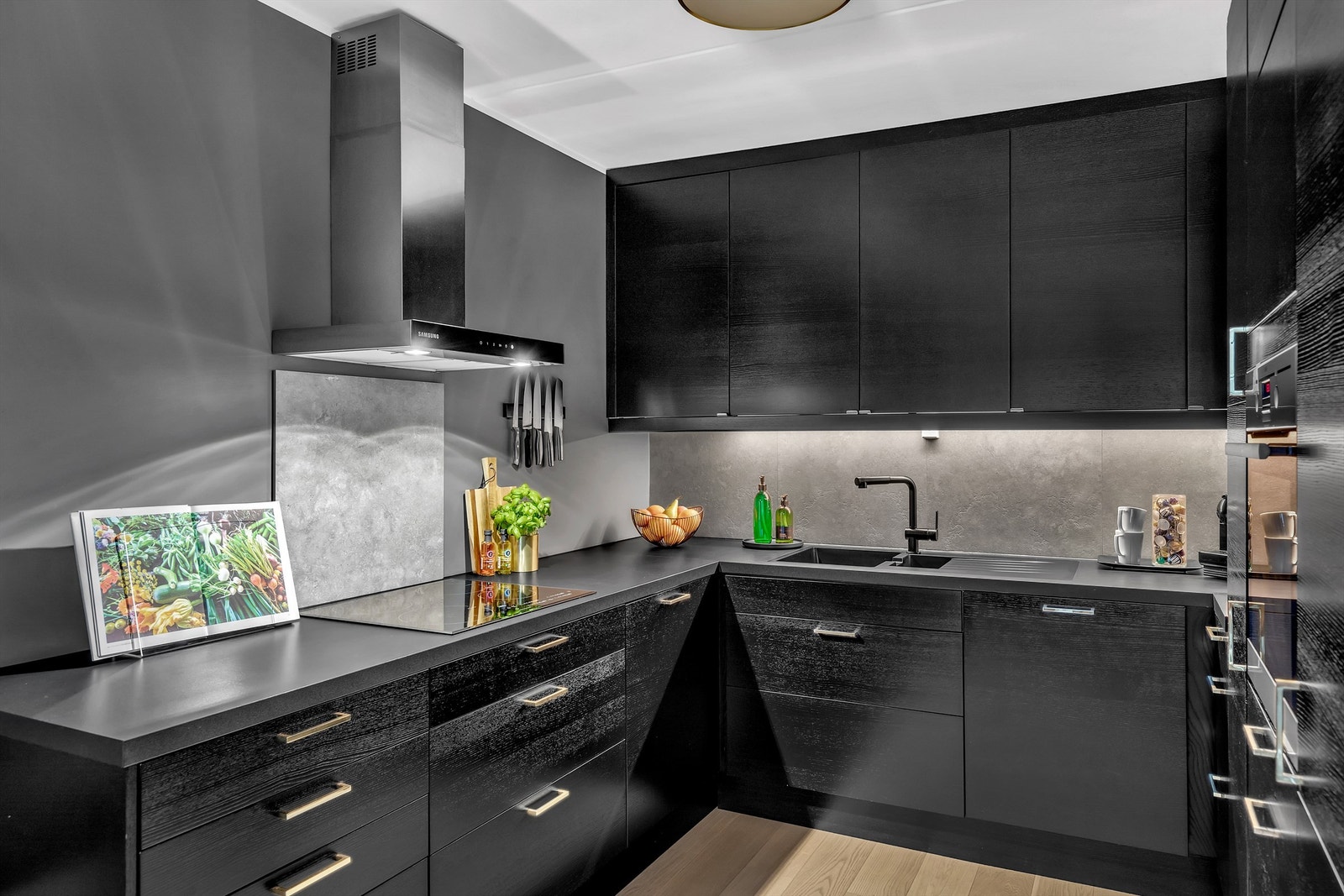 Det er lys under overskap, ventilator over kokeplate, fliser mellom overskap og benk og bak platetopp og nedfelt sort komposittkum og ett-greps blandebatteri. Galleribilde