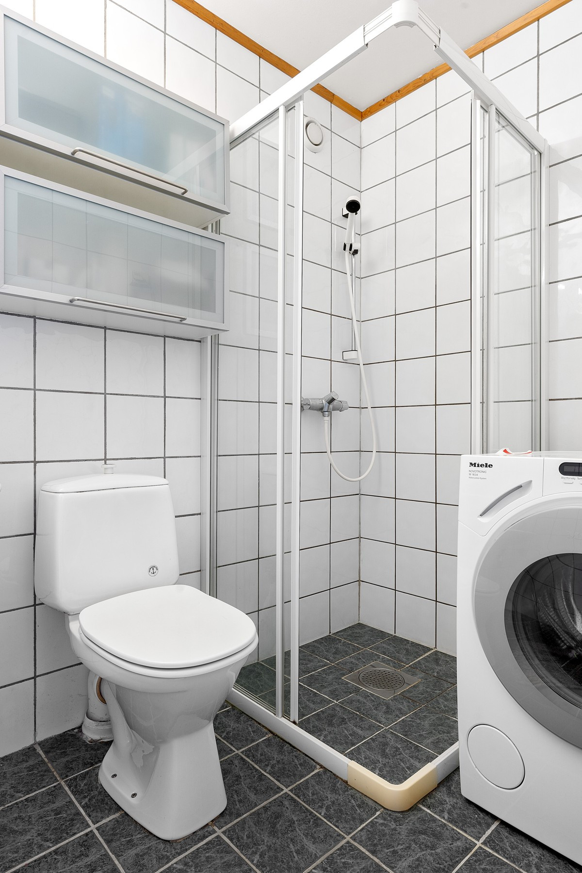 Badet er komplett flislagt med gulvvarme - her er det toalett, dusjhjørne og opplegg for vaskemaksin