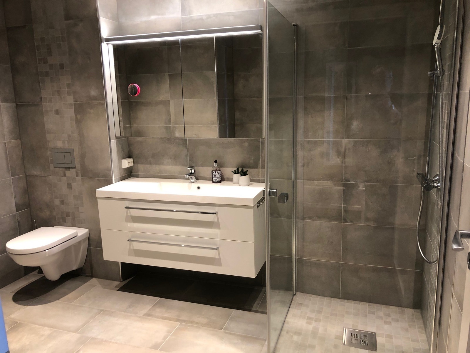 Bad 1. Stort, lekkert flislagt bad med takdusj/hånddusj, vegghengt toalett, romslig servantskap og godt med knagger på veggen til håndklær Galleribilde