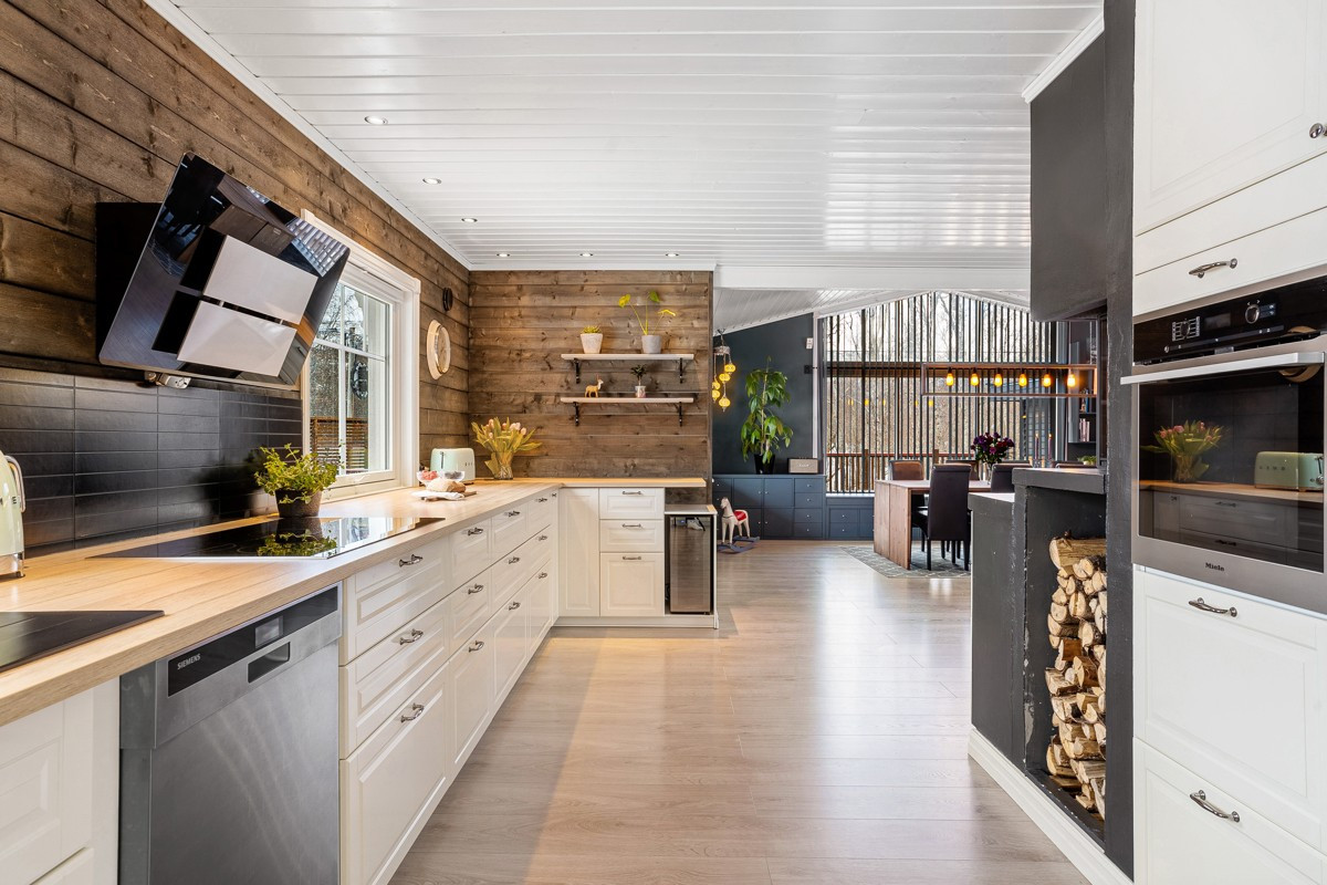 Kjøkkenet fremstår lekkert med de moderne og herskapelige detaljer som med de hvite profilerte frontene, downlights i tak og treverket på vegg.
