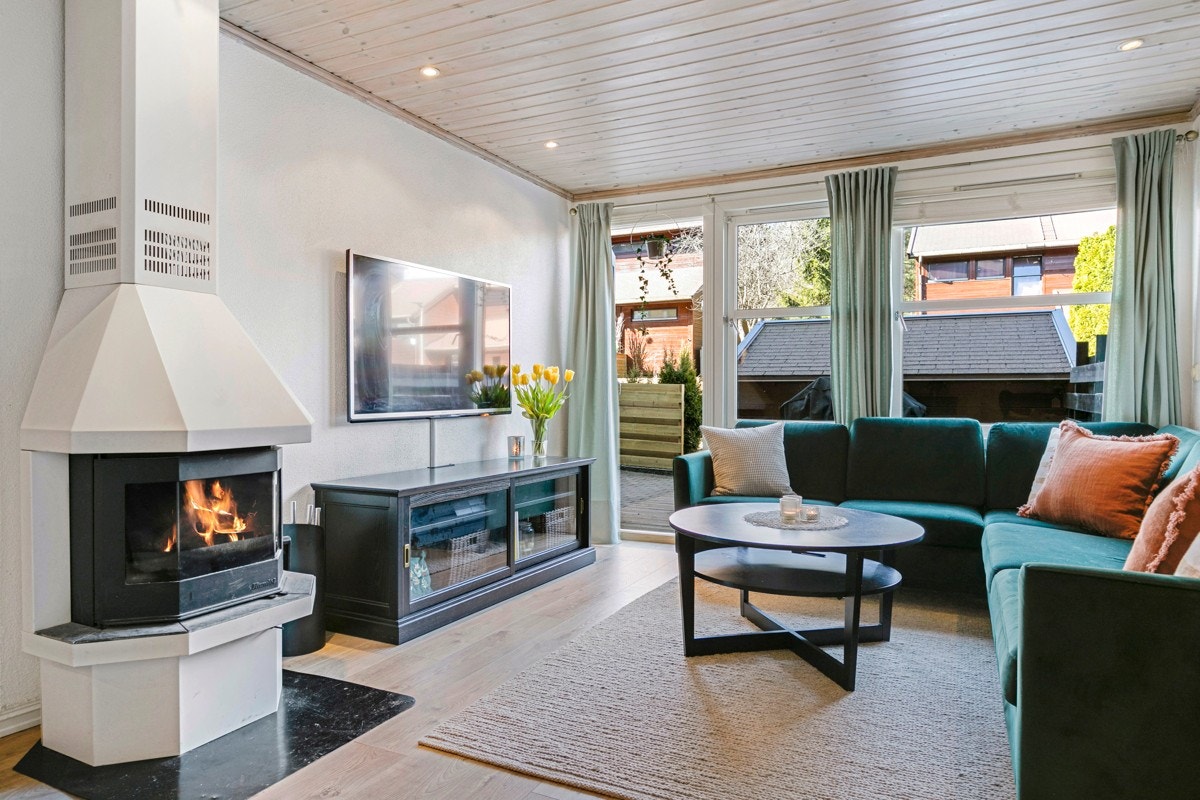 Rikelig med lys fra vinduene og terrassedøren sørger for godt med naturlig daglys i rommet. På kalde dager er det deilig å tenne i peisen og kjenne på varme og kos. Galleribilde