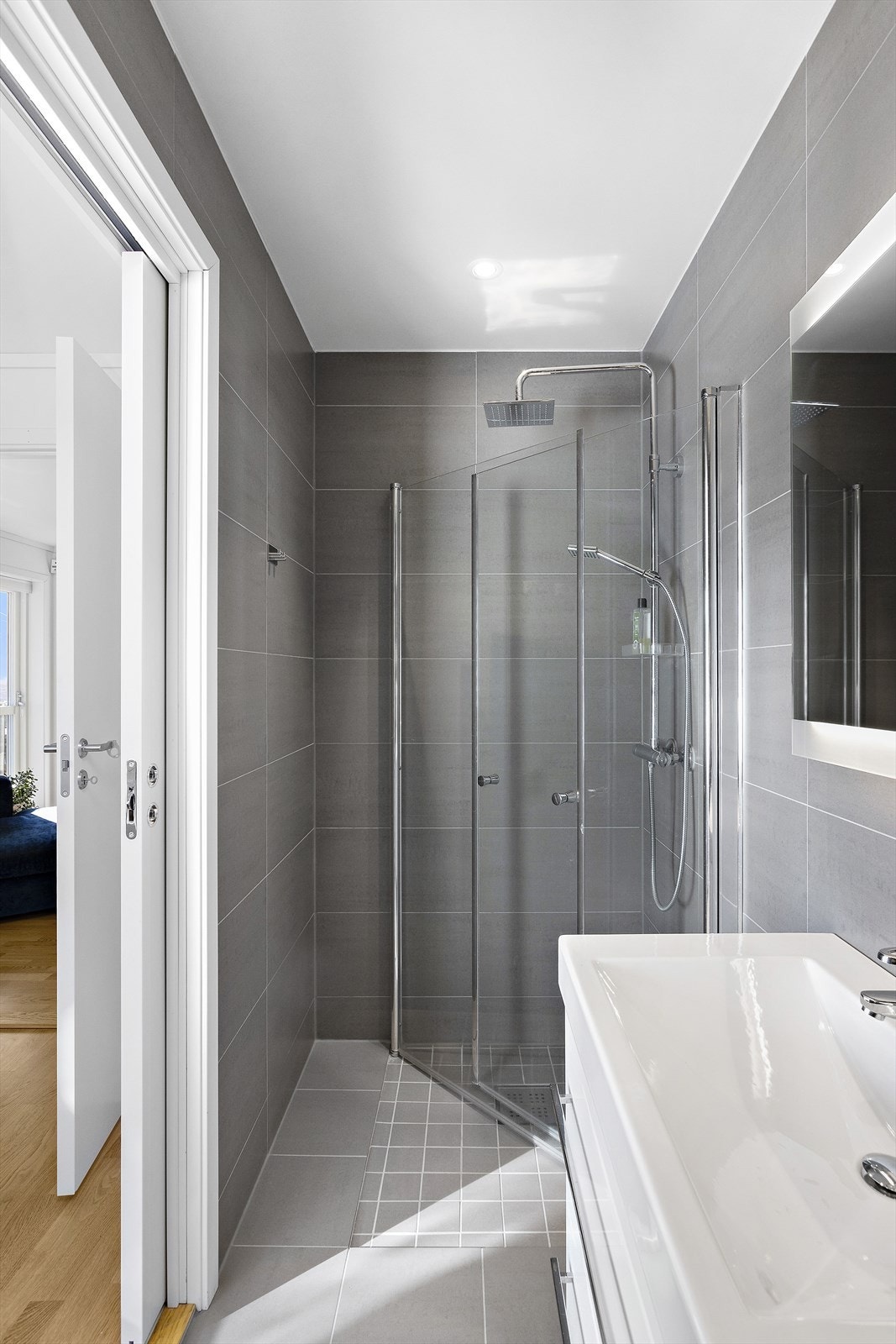 Bad 2 er innredet med dusj med vannfallsdusj, hånddusj og innfellbare glassvegger, helstøpt servant i innredning med skuffer under, speil med belysning samt vegghengt toalett Galleribilde