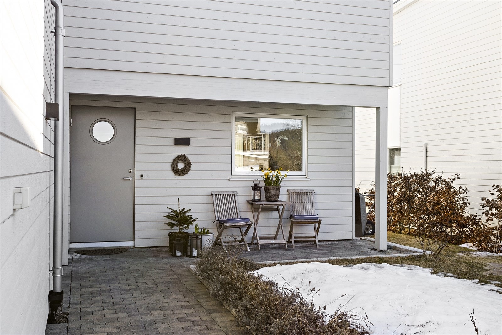 Pent opparbeidet inngangsparti med belegningssten, blomsterbed og hekk mot naboer Galleribilde