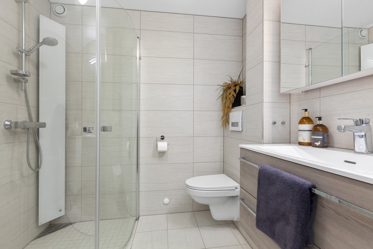 Badet har nedsenket dusjhjørne med innfellbare glassdører, servantinnredning med skuffer, speilskap og opplegg for vaskemaskin m.m. Galleribilde