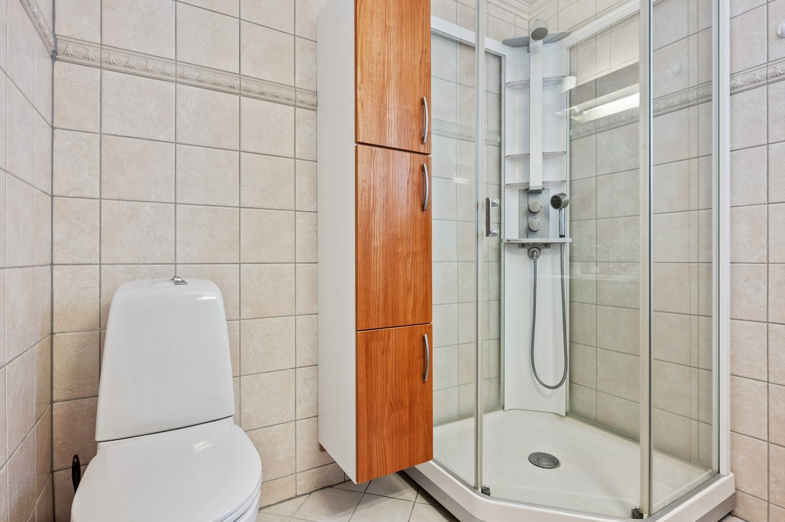 Badet er innredet med en baderomsinnredning med heldekkende servant, speil med overliggende belysning, skap, toalett og dusjkabinett. Galleribilde