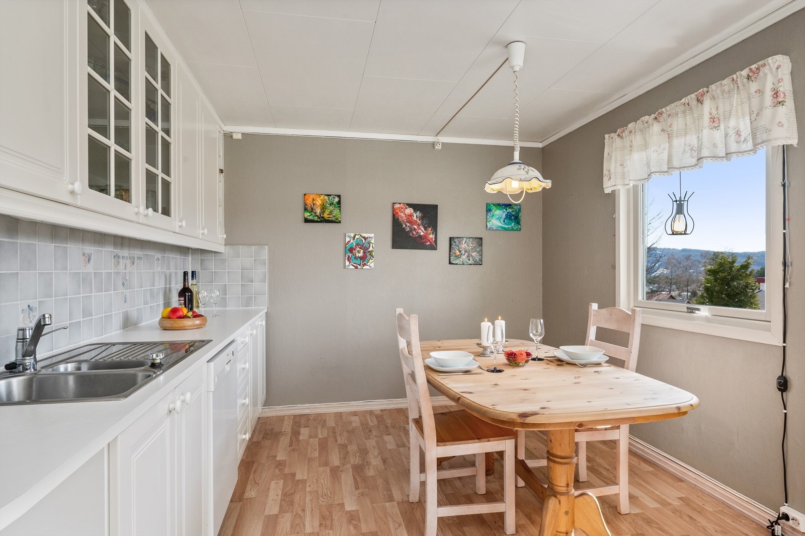 Takhøy kjøkkeninnredning med hvite profilerte fronter, vitrineskap, laminert benkeplate, nedfelt oppvaskkum, avtrekksvifte og fliser over benk. Galleribilde