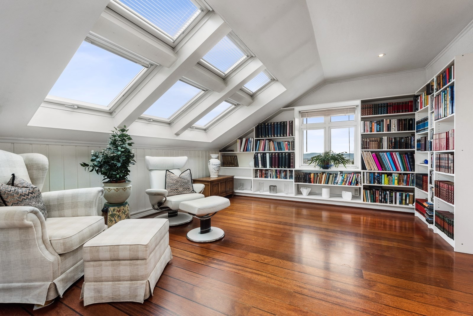 Lyst og koselig bibliotek med store takvinduer og plassbygde bokhyller. Galleribilde