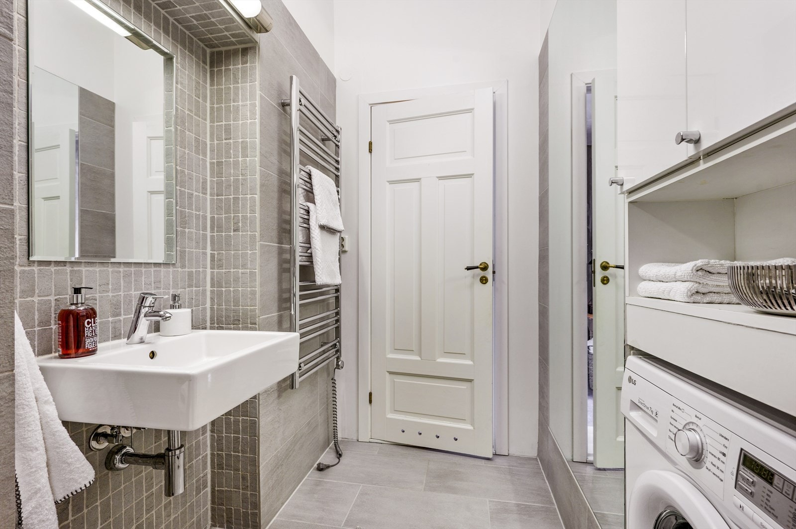 Servantbolle montert på vegg med speil og vask. Opplegg for vaskemaskin samt skap rundt vaskemaskinen og veggmontert klosett. Galleribilde