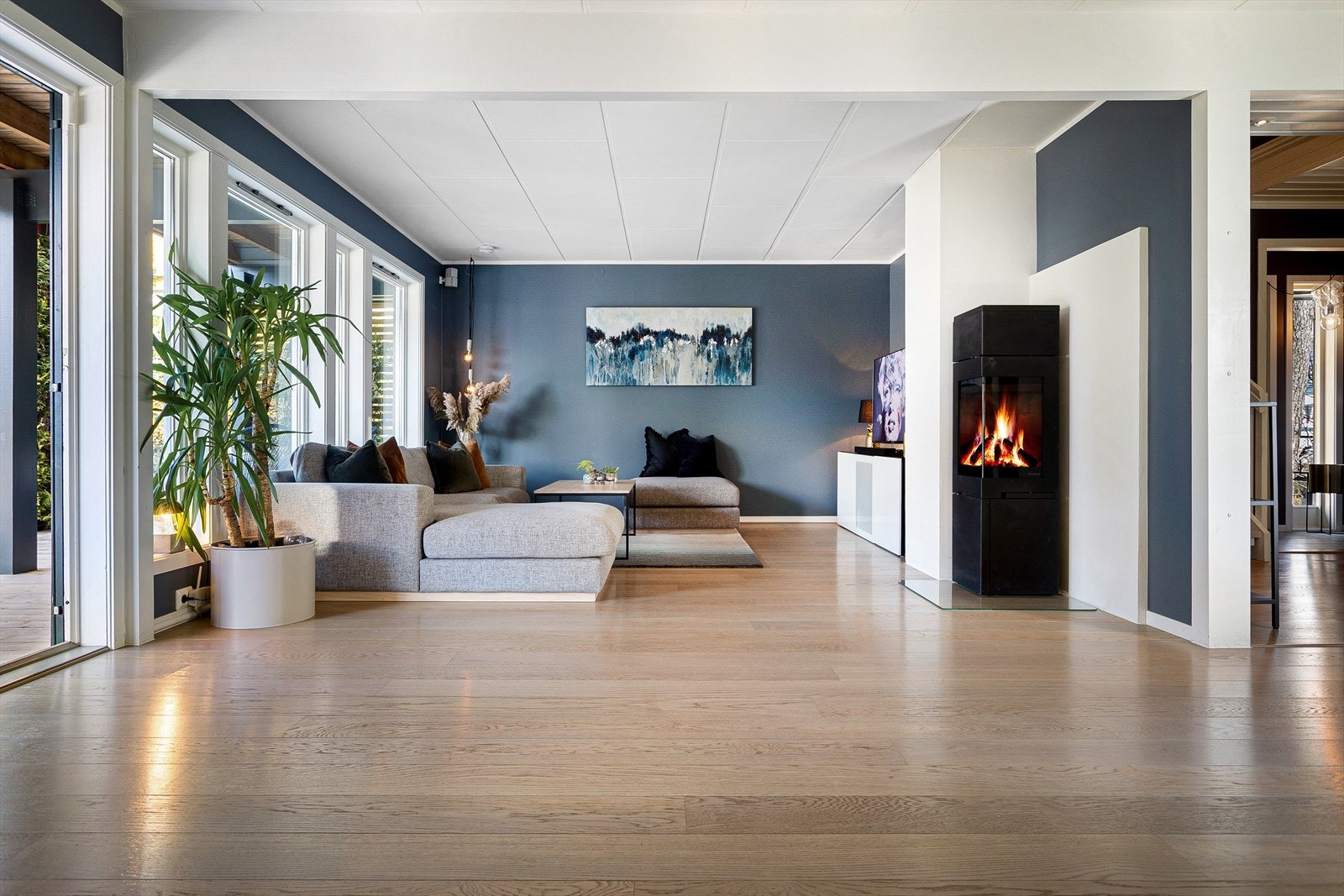 Stor og luftig stue med karnapp malt i moderne farger med rikelig tilgang på naturlig lys. Stuen er naturlig inndelt med plass til flere sittegrupper, spisebord og tilhørende møbler. Det er montert en peisovn i stuen fra Norpeis. Galleribilde