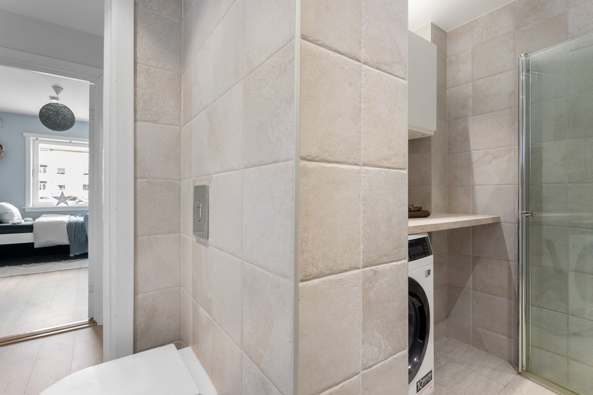 Baderommet inneholder dusjsone med hånd- og regndusj, toalett, vegghengt servantskap, speilskap og opplegg for vaskemaskin. Galleribilde