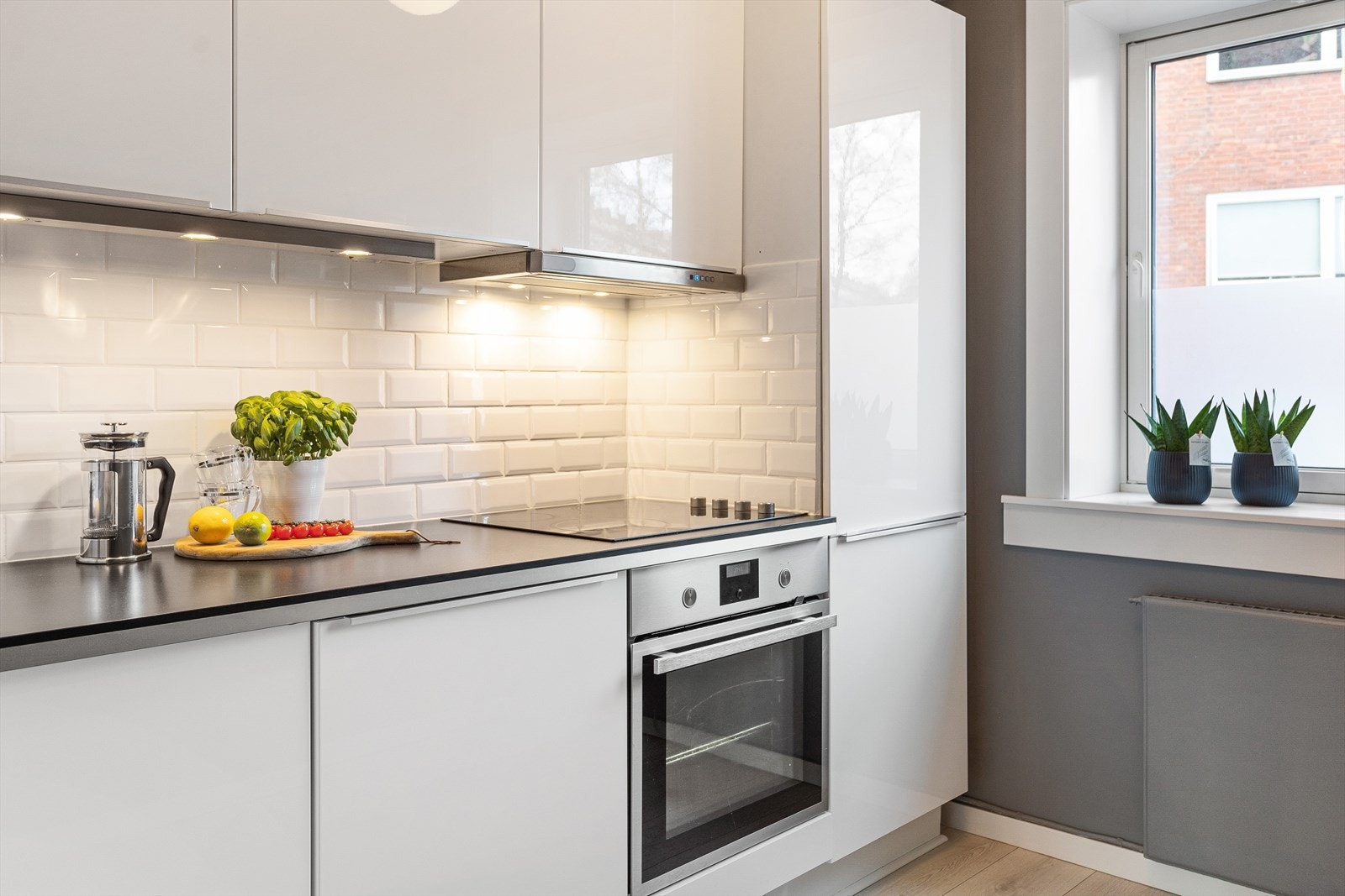 Flislagt mellom benkeplate og overskap, lysarmatur under overskap samt stikkontakt på vegg. Galleribilde