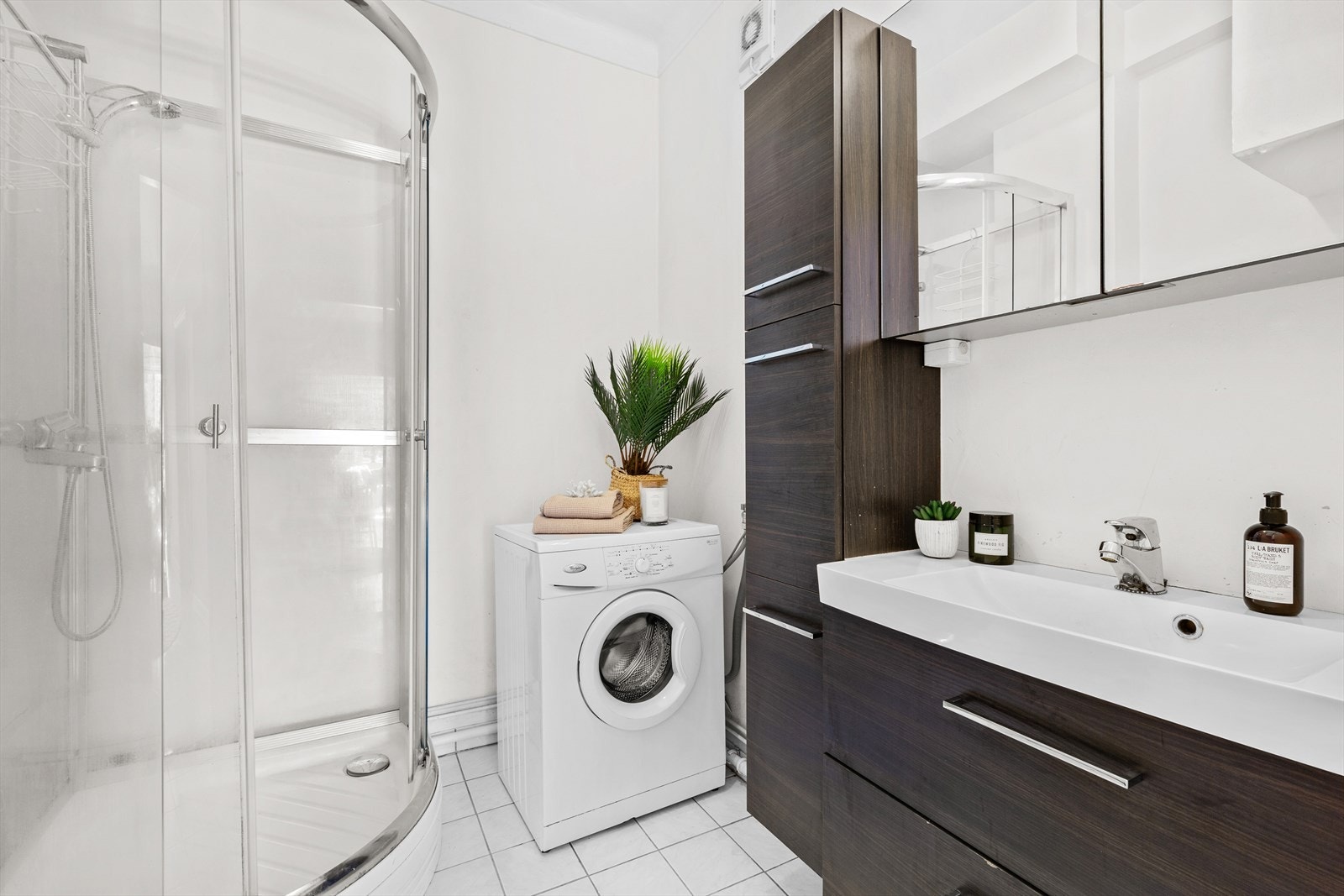 Lyst baderom med flislagt gulv med varme. Skap med speil samt belysning over servant. med gode oppbevaringsmuligheter. Vegghengt servantskap i slett utførelse med gode oppbevaringsmuligheter. Dusjkabinett med skyvedør og frittstående toalett. Galleribilde