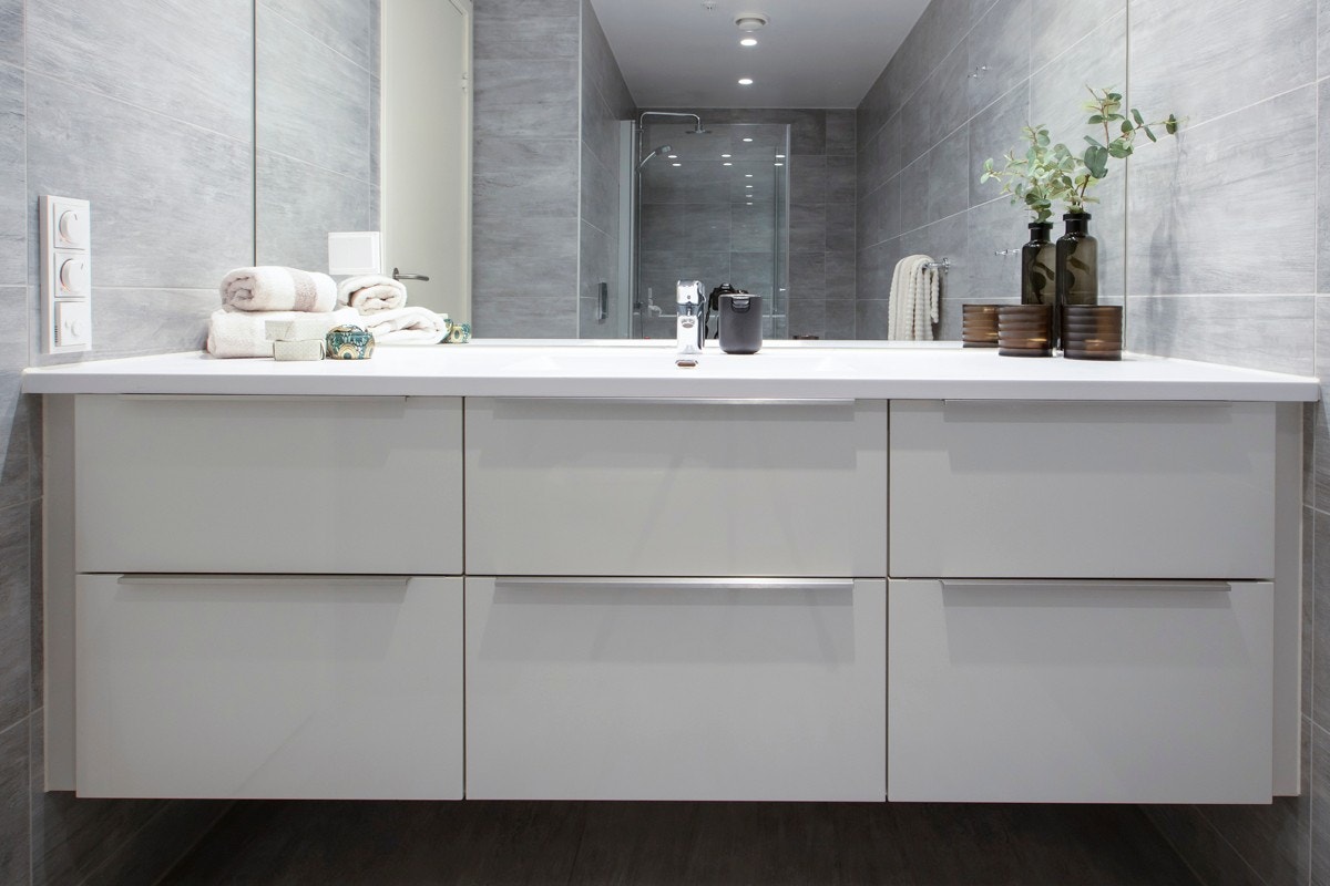 Master-badet har lyse fliser på overflater, med varme i gulv, og det er downlights i tak. Rommet har høyglanset servantskap, speil, vegghengt toalett og et dusjhjørne med regnfallsdusj og rette dører i herdet glass. Galleribilde