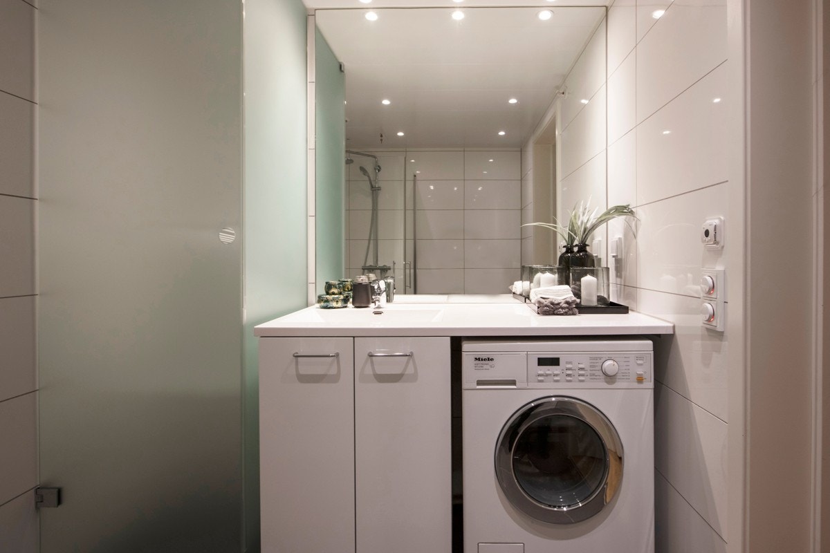 Det andre badet har mørke grå gulvfliser, hvite veggfliser, downlights og gulvvarme. Rommet har speil, servantskap med benkeplate som danner nisje til vaskemaskin. I tillegg er det et tørkeskap dusj og vegghengt toalett. Galleribilde