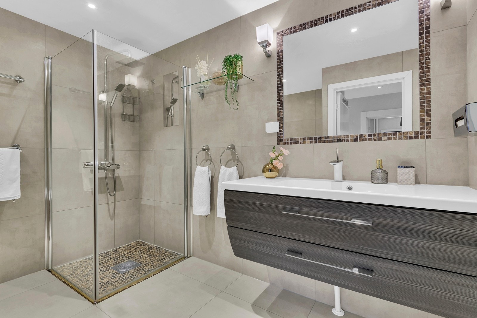 Badet er utstyrt med heldekkende servant på underskap, speil og dusj med dusjvegger i herdet glass og innfliset badekar. Galleribilde